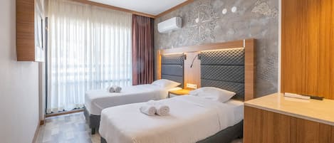 A hotel room with two beds, a wooden headboard, a wall-mounted air conditioner, and a large window with curtains.