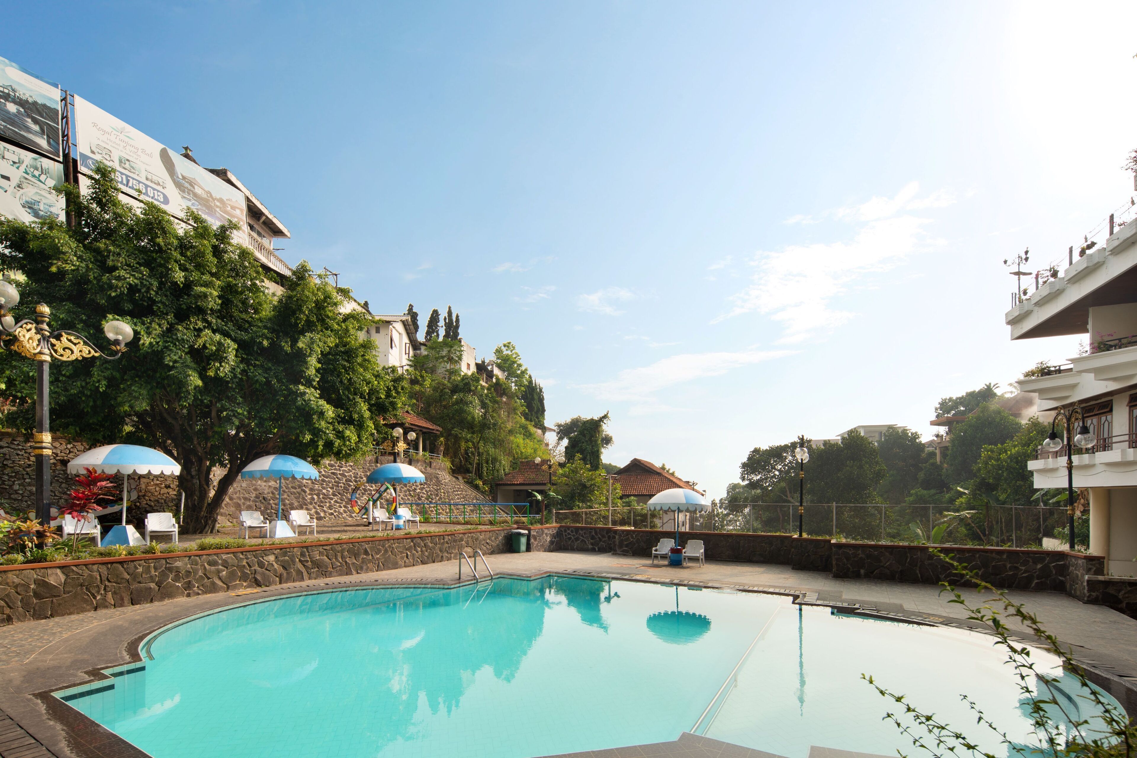 Ein Swimmingpool mit Liegestühlen und Sonnenschirmen, umgeben von Steinmauern und Grünpflanzen.