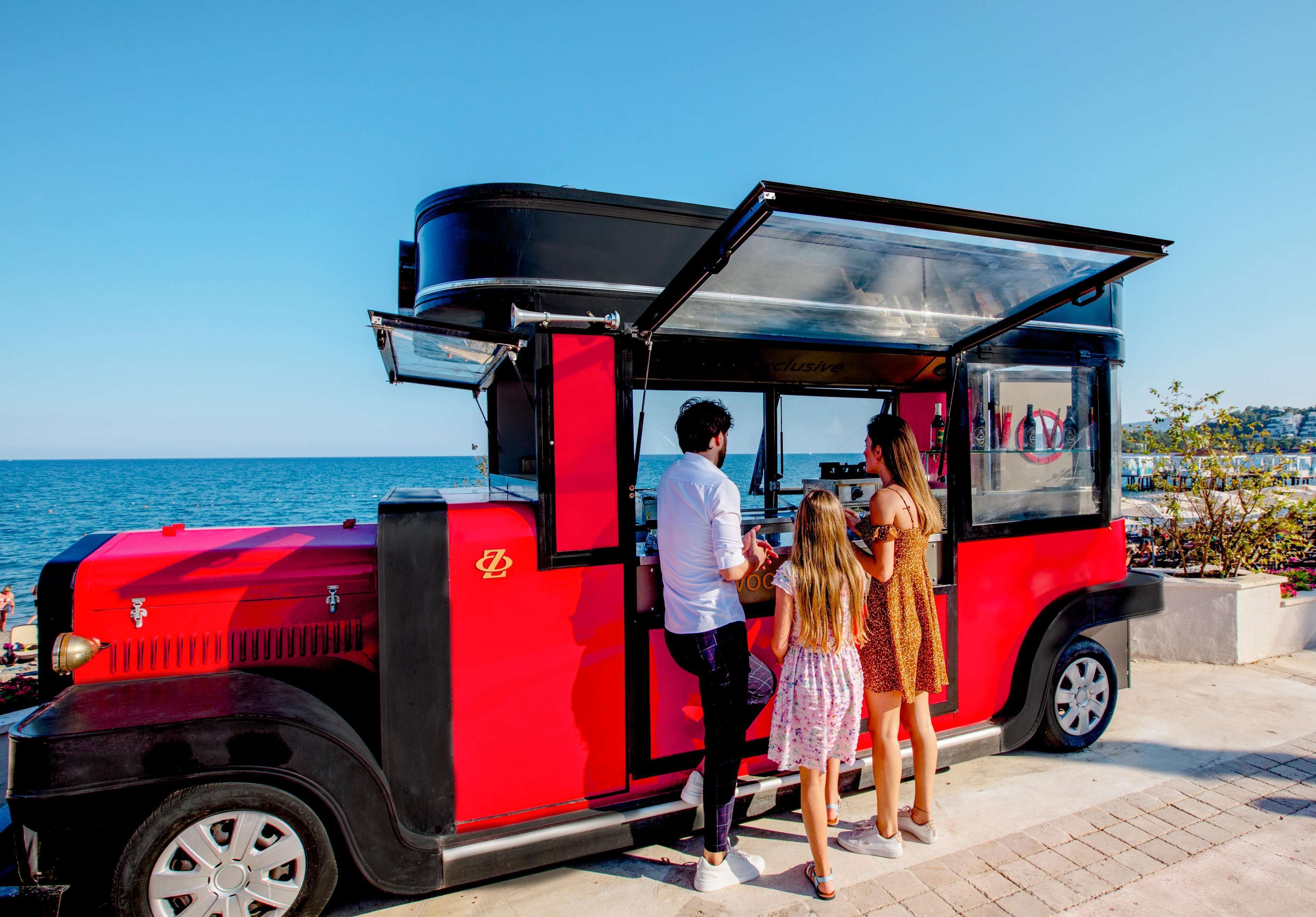 Ein roter Food-Truck mit einer durchsichtigen Plane, in der Nähe eines Uferbereichs.