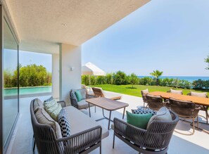 A spacious outdoor patio with wicker furniture, a wooden table, and a view of the sea. - Sherwood Exclusive Kemer (Kemer)
