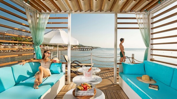 A deck with blue seating, a table with a fruit bowl, and a view of the sea and a pier. - Sherwood Exclusive Kemer (Kemer)