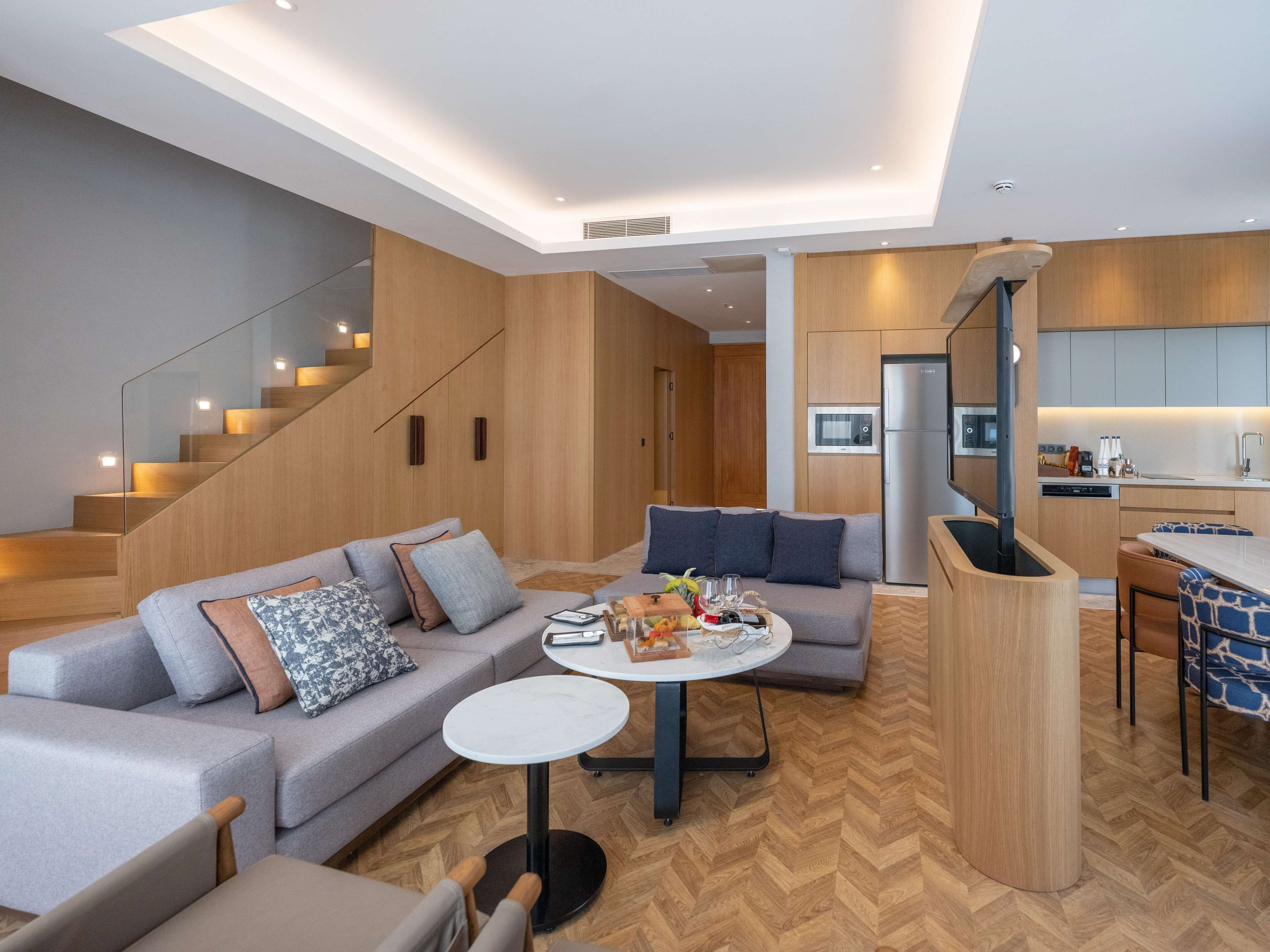A modern living room with a grey sofa, a round coffee table, and a staircase leading to a kitchen area.