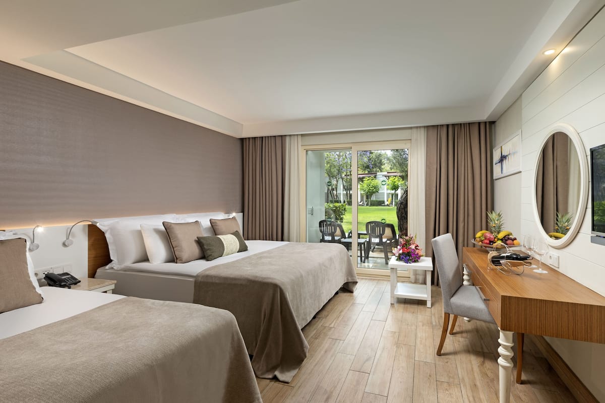 A hotel room with two beds, a wooden desk, a chair, a dining table, a telephone, and a large window with curtains.