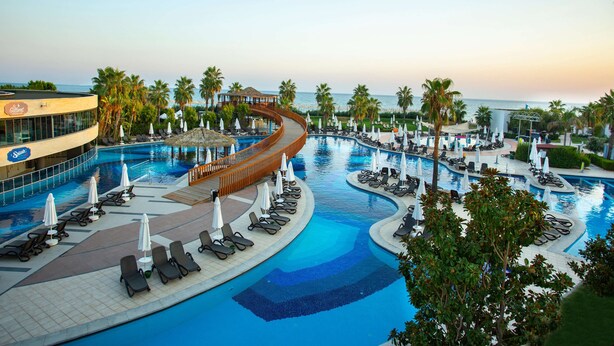 Zona de piscina de un complejo turístico con varias piscinas, sillones de descanso y sombrillas.
