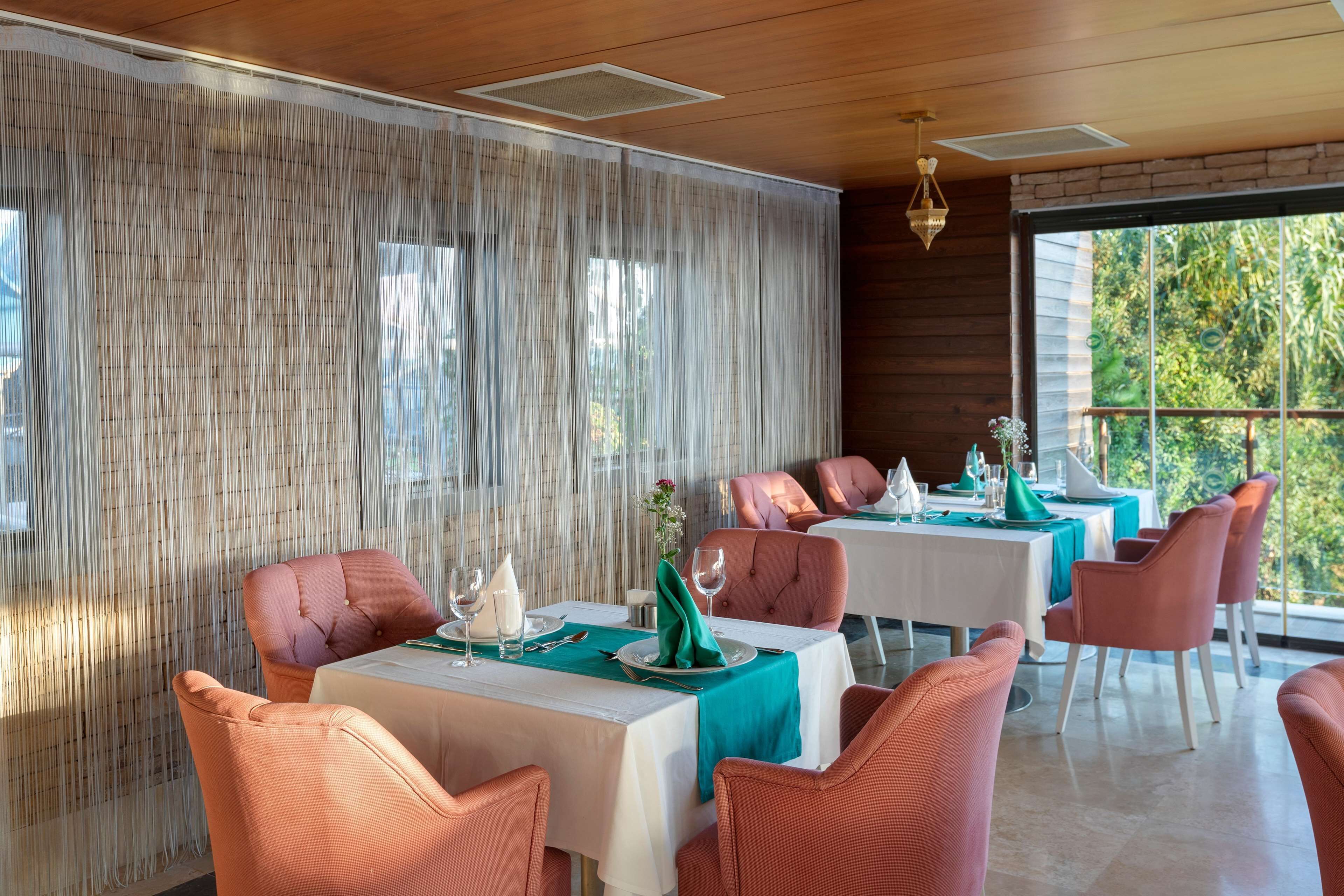 A dining area with tables set for four, each with pink chairs and teal tablecloths.