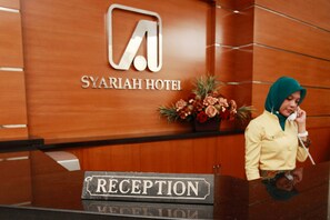 Un comptoir d’accueil avec une enseigne indiquant « SYARIAH HOTEL » et, en dessous, « RÉCEPTION ».