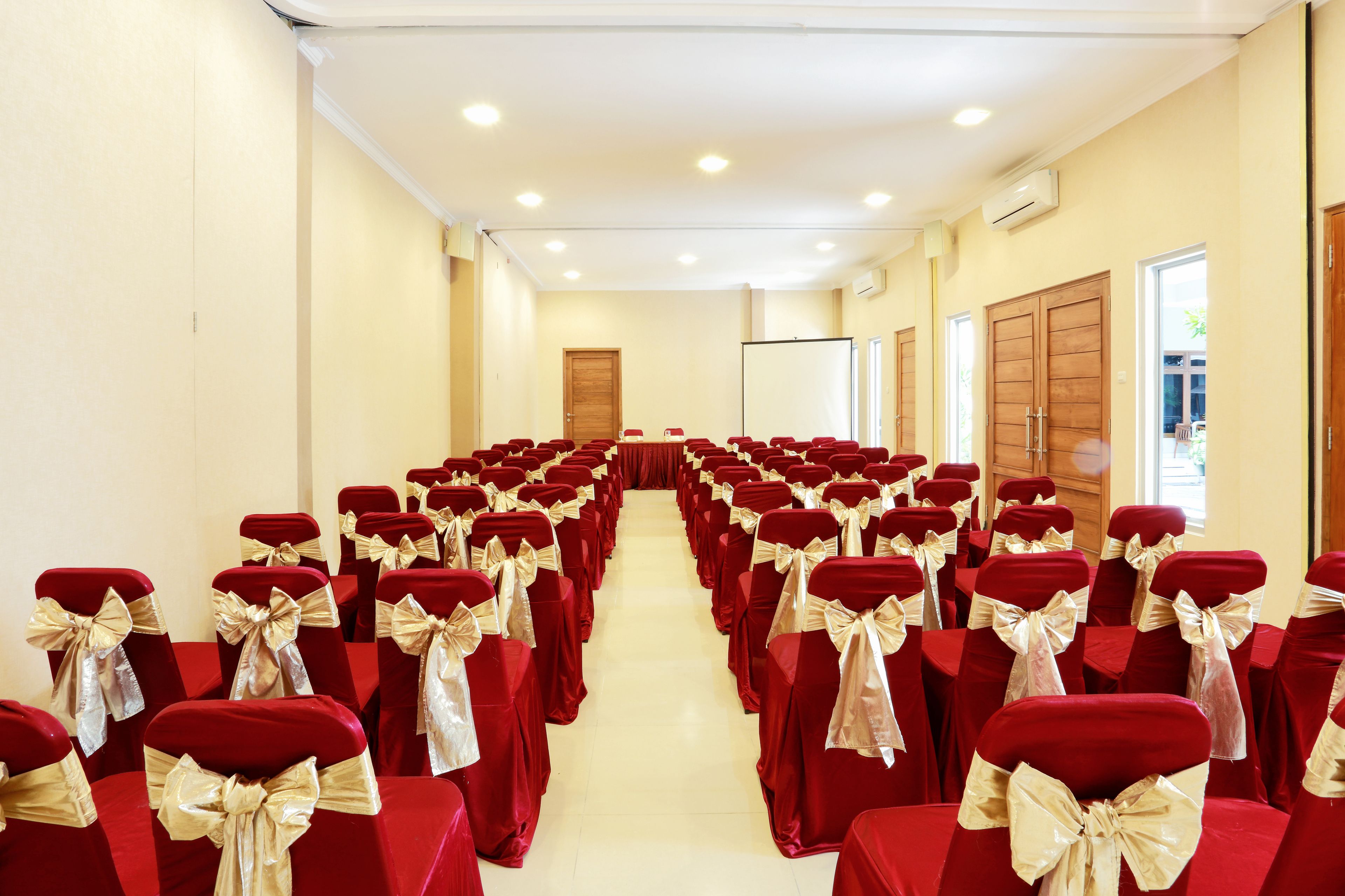 A conference room with rows of red chairs with gold sashes, a whiteboard, and a projector screen.