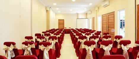 A conference room with rows of red chairs with gold sashes, a whiteboard, and a projector screen.