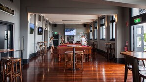 Un grand espace bar doté d’un plancher en bois, de hauts tabourets et d’une table de billard au centre.