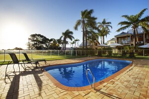 Una piscina al aire libre, sombrillas, sillones reclinables de piscina