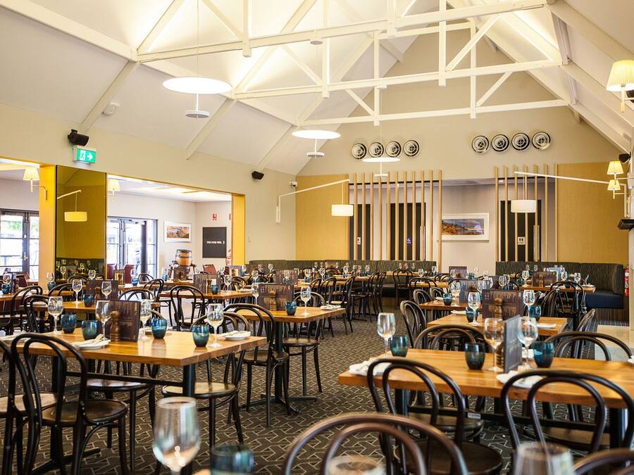 A spacious restaurant with multiple tables and chairs, high ceilings, and modern lighting fixtures.