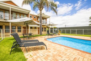 Una piscina al aire libre, sombrillas, sillones reclinables de piscina