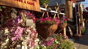 Un letrero de madera dice 'Log Home Boutique House & Cafe', con cestas de mimbre llenas de flores.