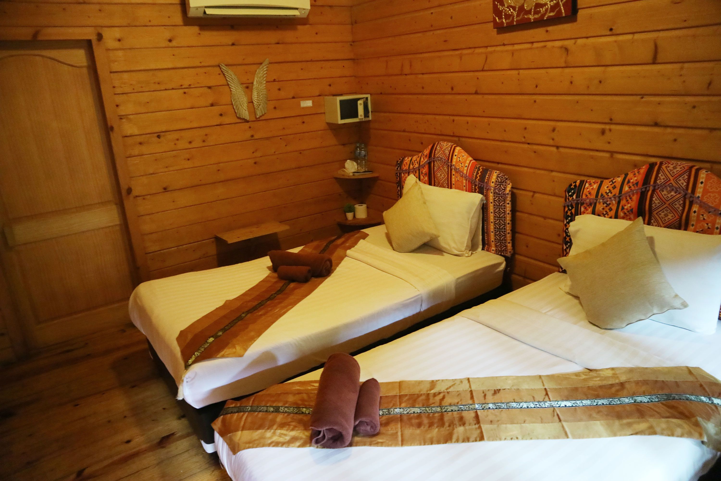 A wooden cabin room with two beds, a small table, a wall-mounted TV, and a door.