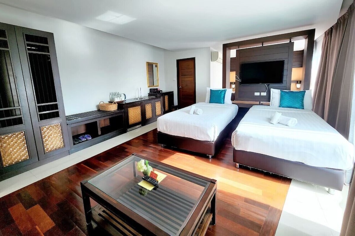 A hotel room with two beds, a TV, a minibar, and a seating area with a coffee table.