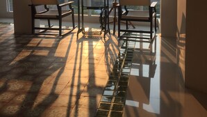 Una habitación iluminada por el sol con vistas a edificios a través de amplias ventanas, una mesa con sillas y una lámpara colgante.