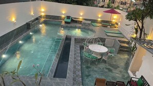 Un área de piscina en la azotea con un jacuzzi, sillas de descanso y una mesa de comedor con sillas.