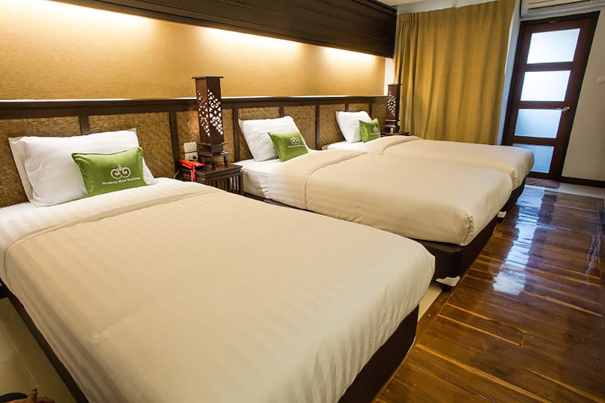 A hotel room with three beds, each with white linens and green pillows, wooden headboards, and a wooden floor.