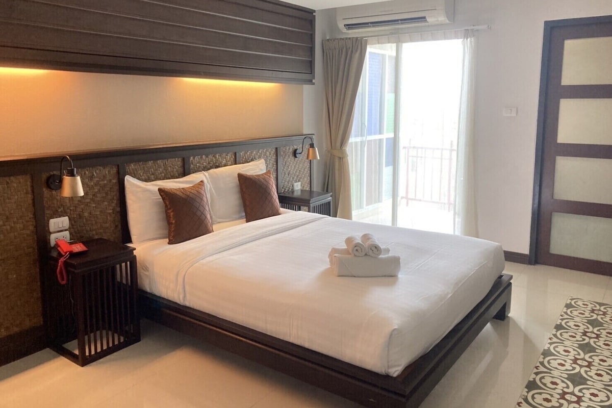 A hotel room with a large bed, a nightstand, an air conditioning unit, a view of the outside, and a sliding door.