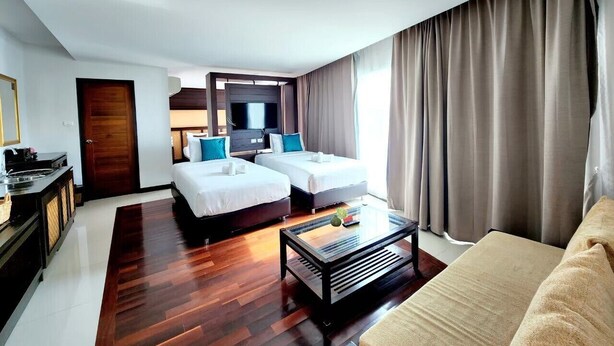 Una habitación de hotel con dos camas, un sofá, una mesita de café, un televisor y un armario de madera.