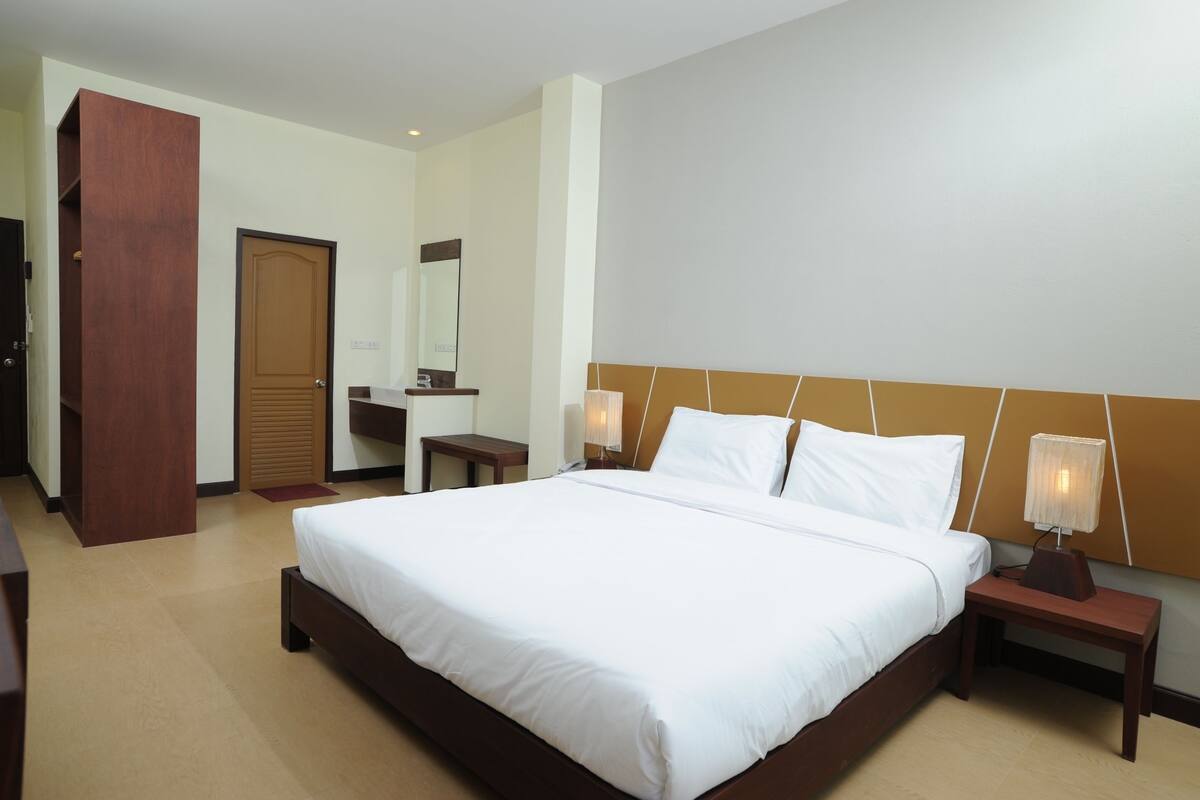 A hotel room with a large bed, a wooden headboard, a nightstand with a lamp, a mirror, and a wardrobe.