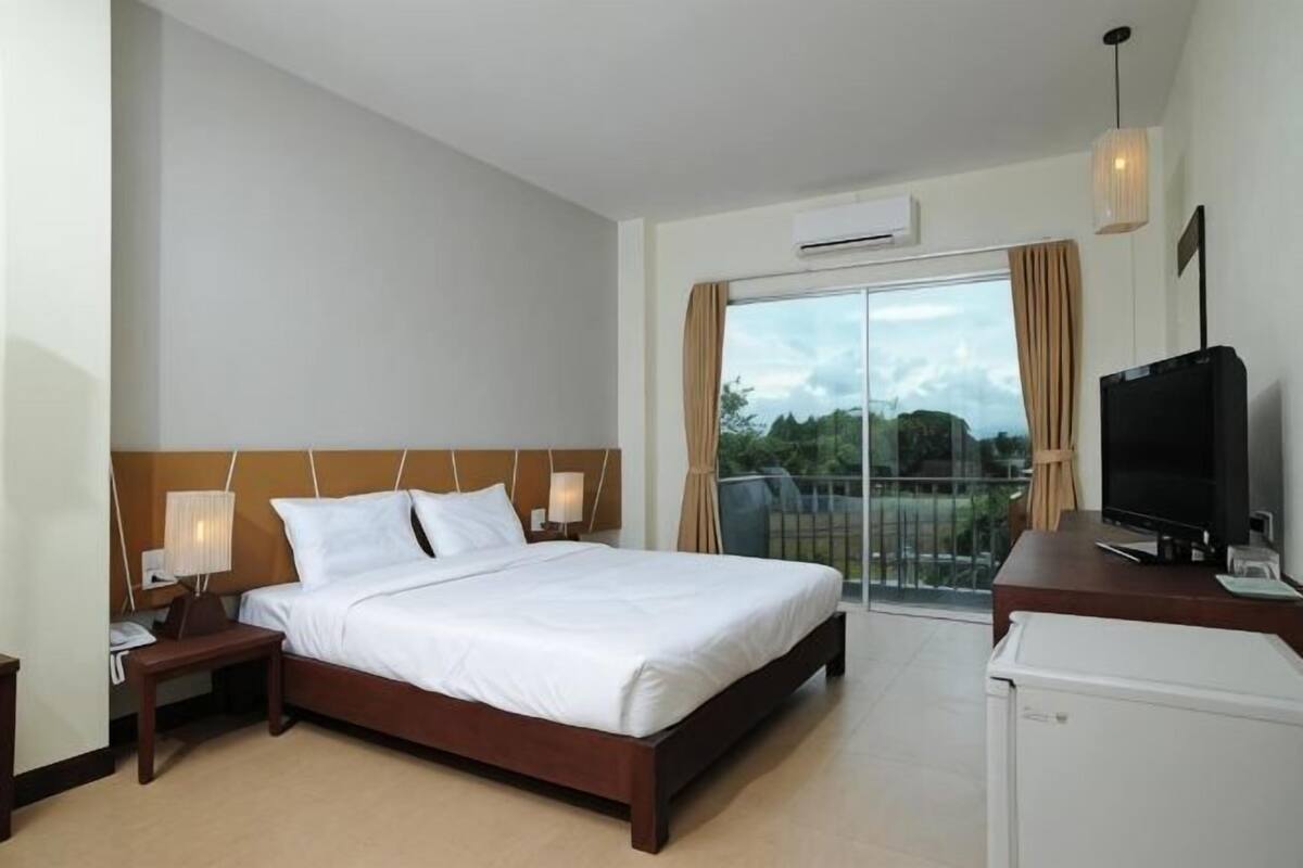 A hotel room with a bed, a TV, a desk, and a balcony with a view.