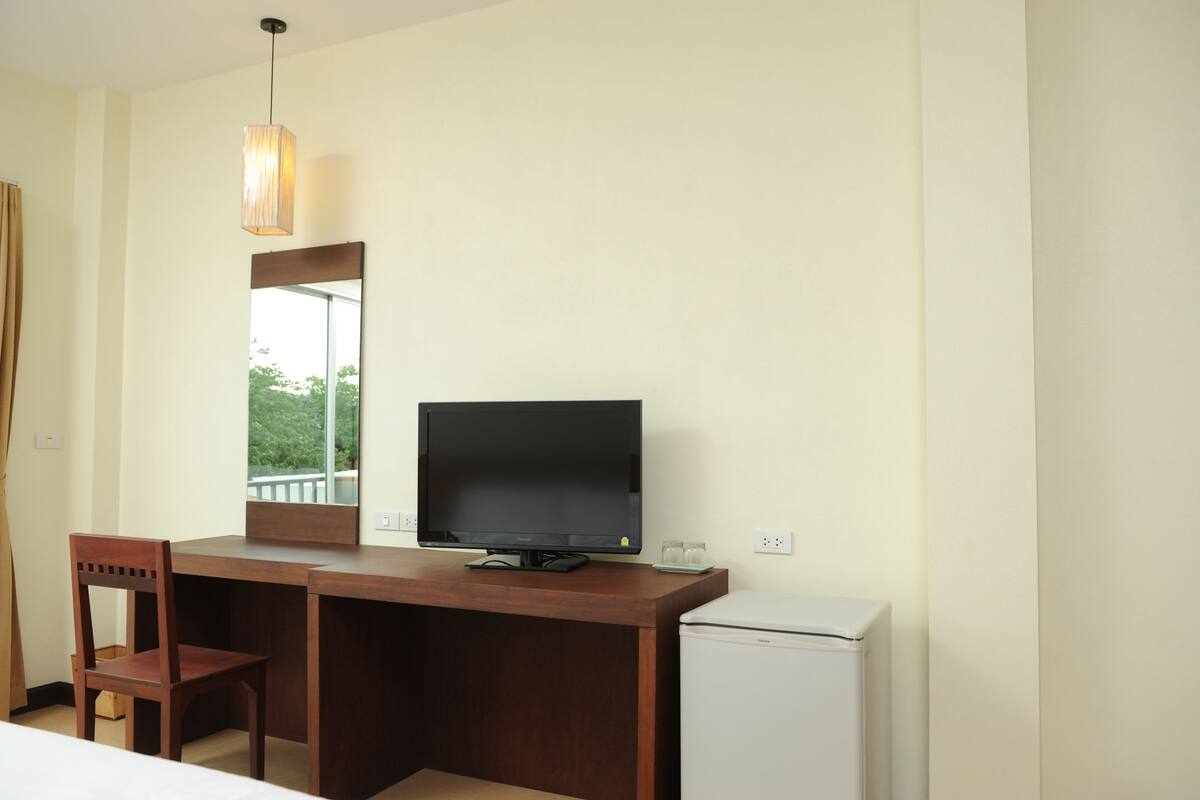 A hotel room with a wooden desk, a television, a small refrigerator, and a chair.