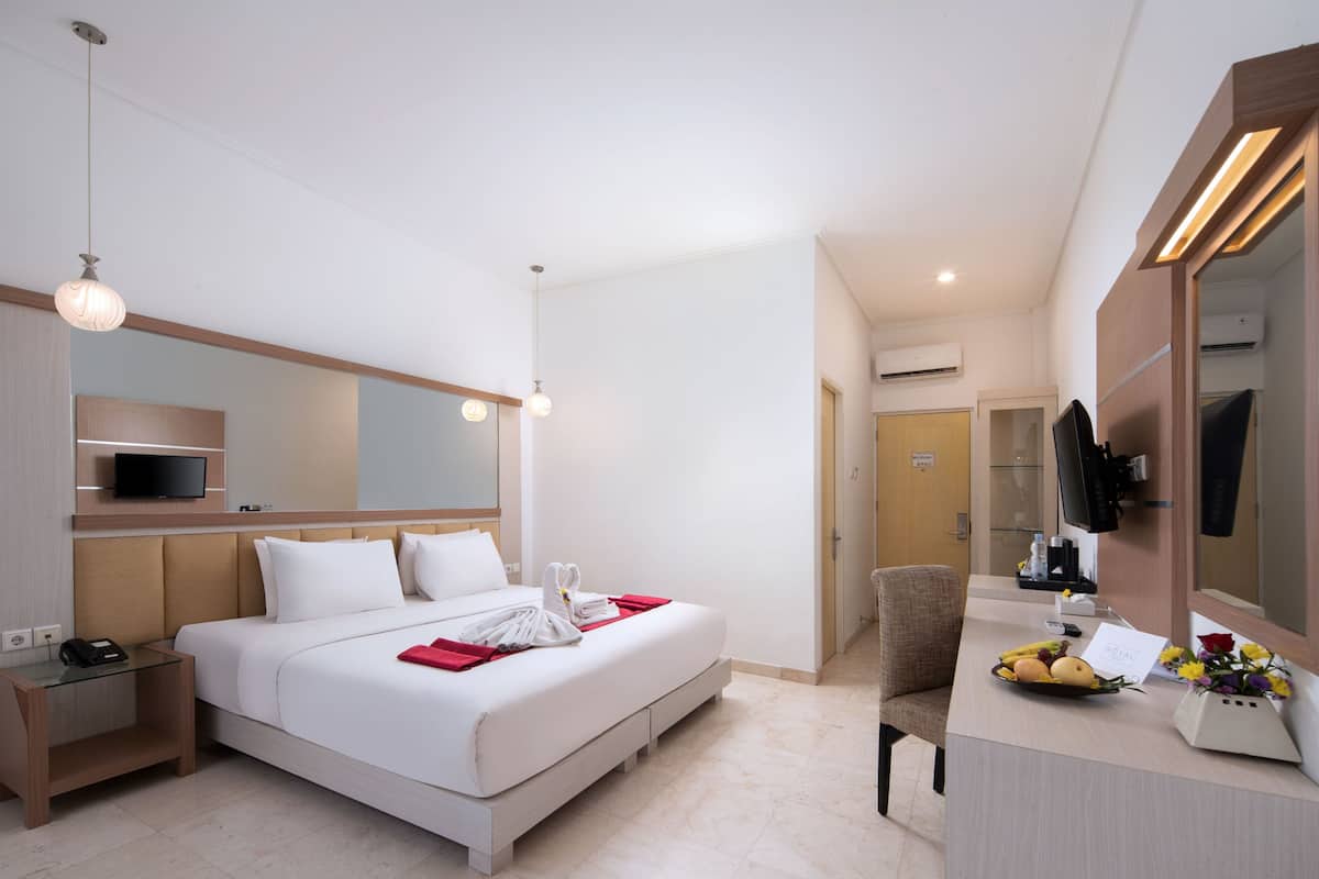 A hotel room with a bed, bedside table, TV, and a desk with a mirror.