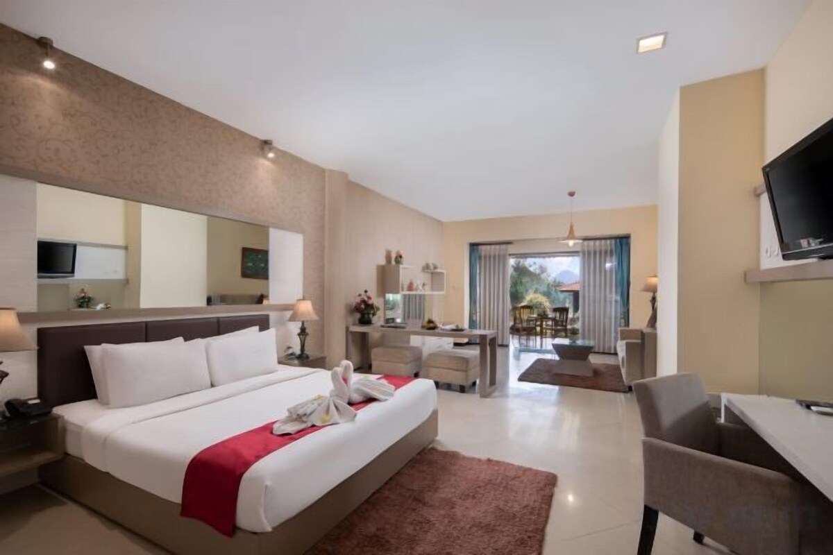 Ein Hotelzimmer mit einem großen Bett, einem Schreibtisch, einem Sessel, einem Fernseher und einem durch eine offene Tür einsehbaren Badezimmer.