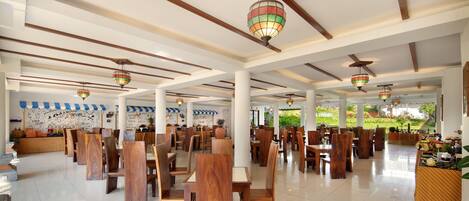 A spacious restaurant with wooden tables and chairs, hanging decorative lights, and a mural on the wall.