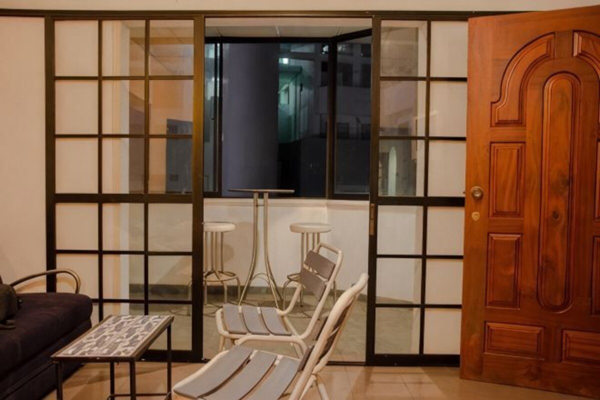 A room with a sliding glass door, a wooden door, a sofa, two chairs, and a small table.