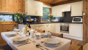 A wooden interior with a dining table set for four, white cabinets, a microwave, and an oven. - Brockwood Hall (Millom)