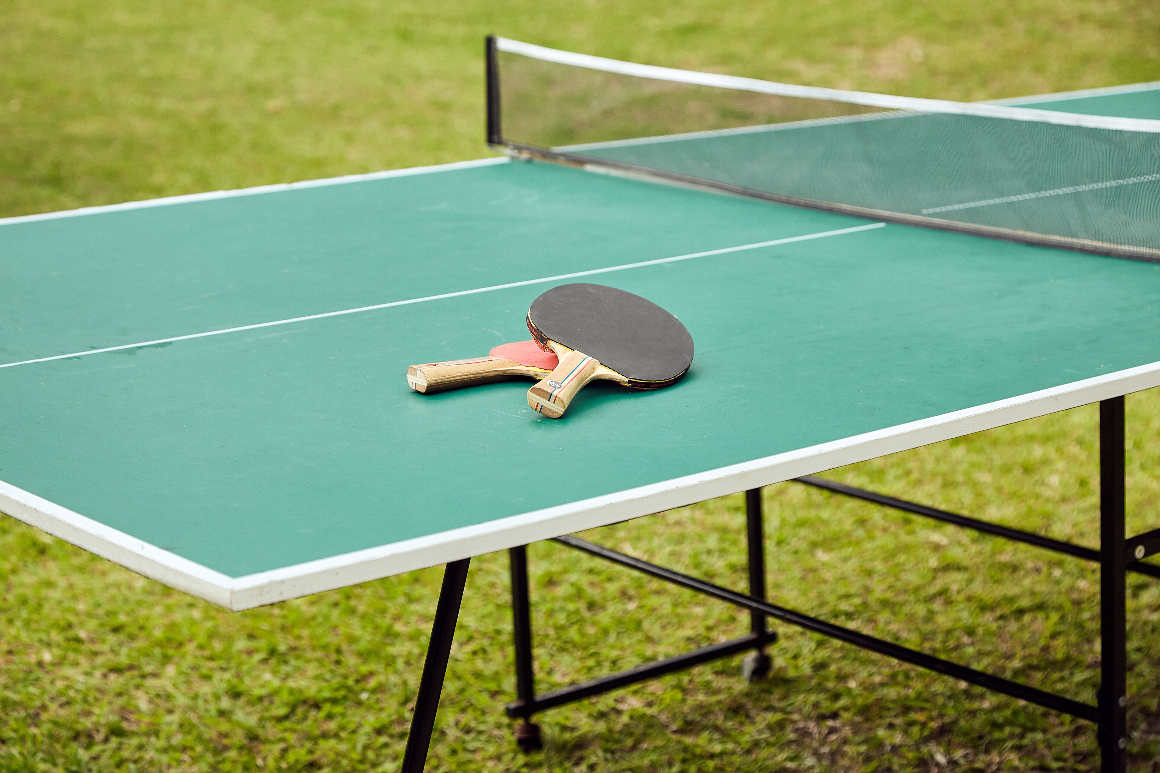 A green ping pong table with a net and two paddles on it.
