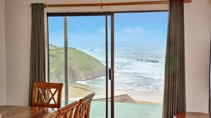 A room with a wooden table and chairs, a view of the ocean through a sliding glass door, and a beach visible through the door. - First Group Hole in the Wall (King Sabata Dalindyebo)