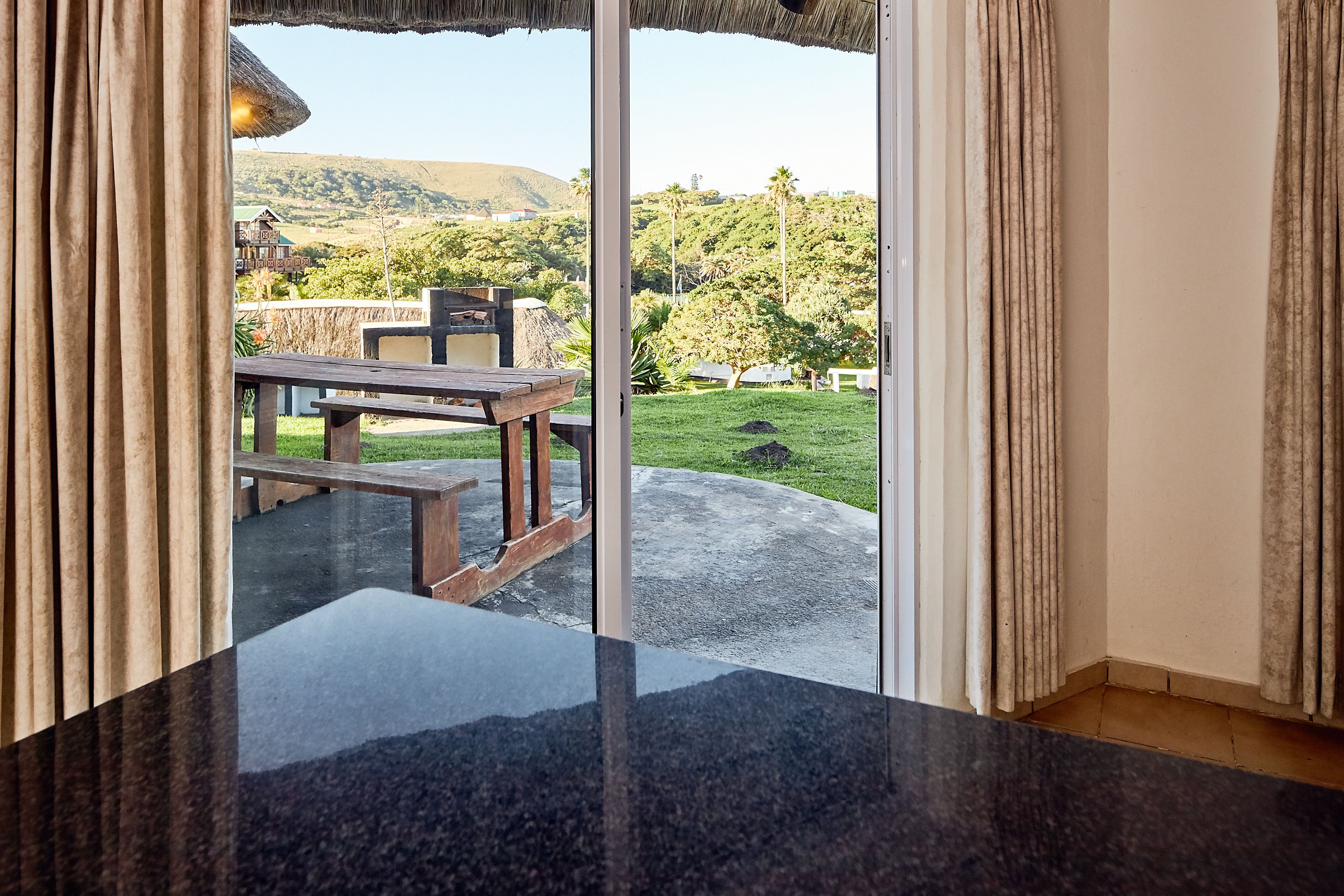 A room with a sliding glass door leading to an outdoor area with a picnic table and a grassy lawn.