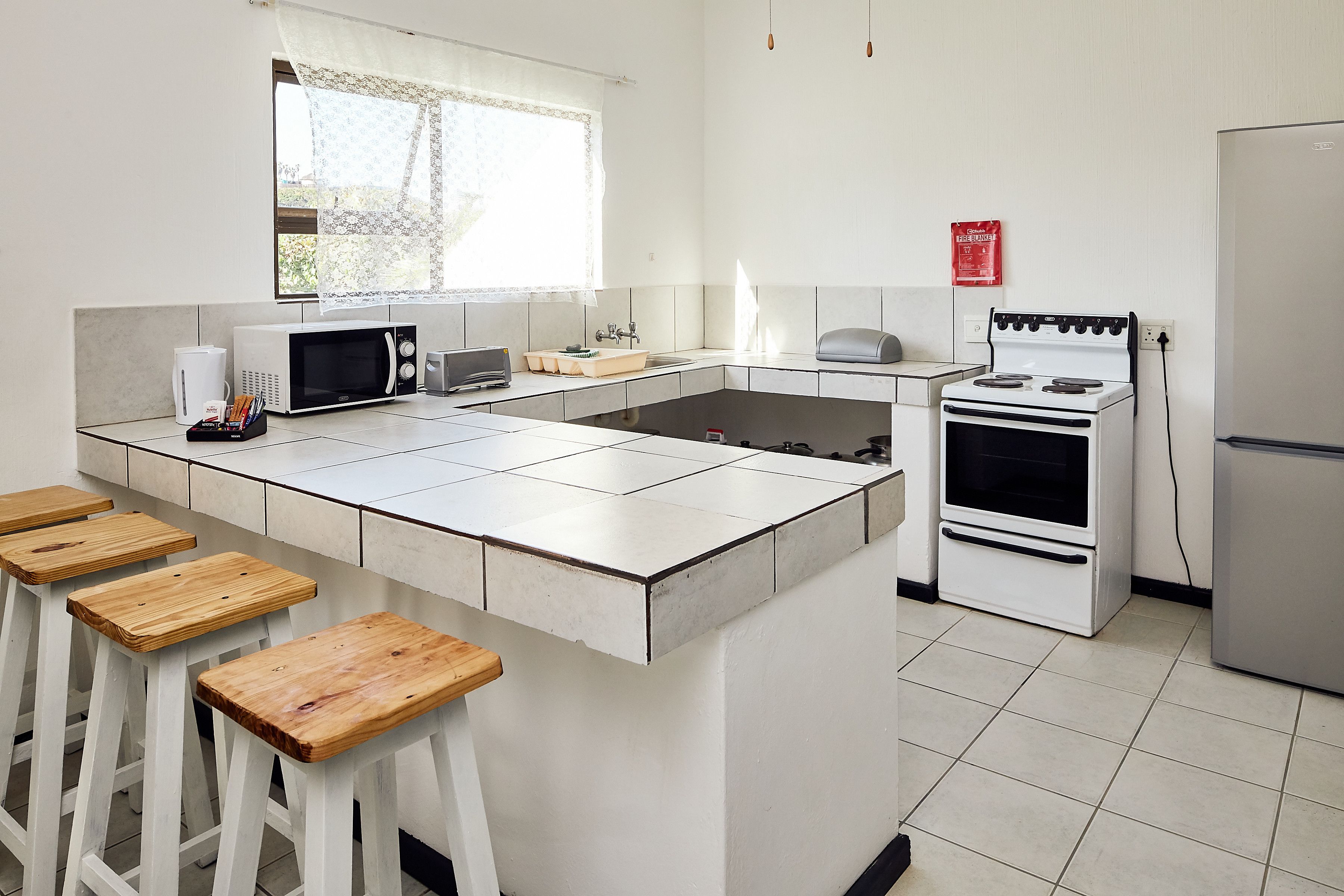Eine moderne Küche mit einer zentralen Kochinsel, weißen Schränken, einer Mikrowelle, einem Toaster und einem Herd. Um die Insel herum stehen Holzstühle.