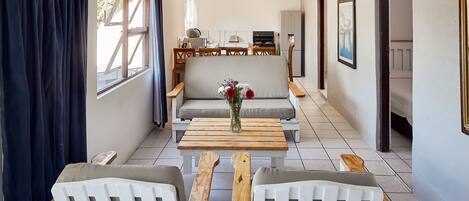 A modern, well-lit room with a sofa set, wooden chairs, a coffee table, and a kitchen in the background.