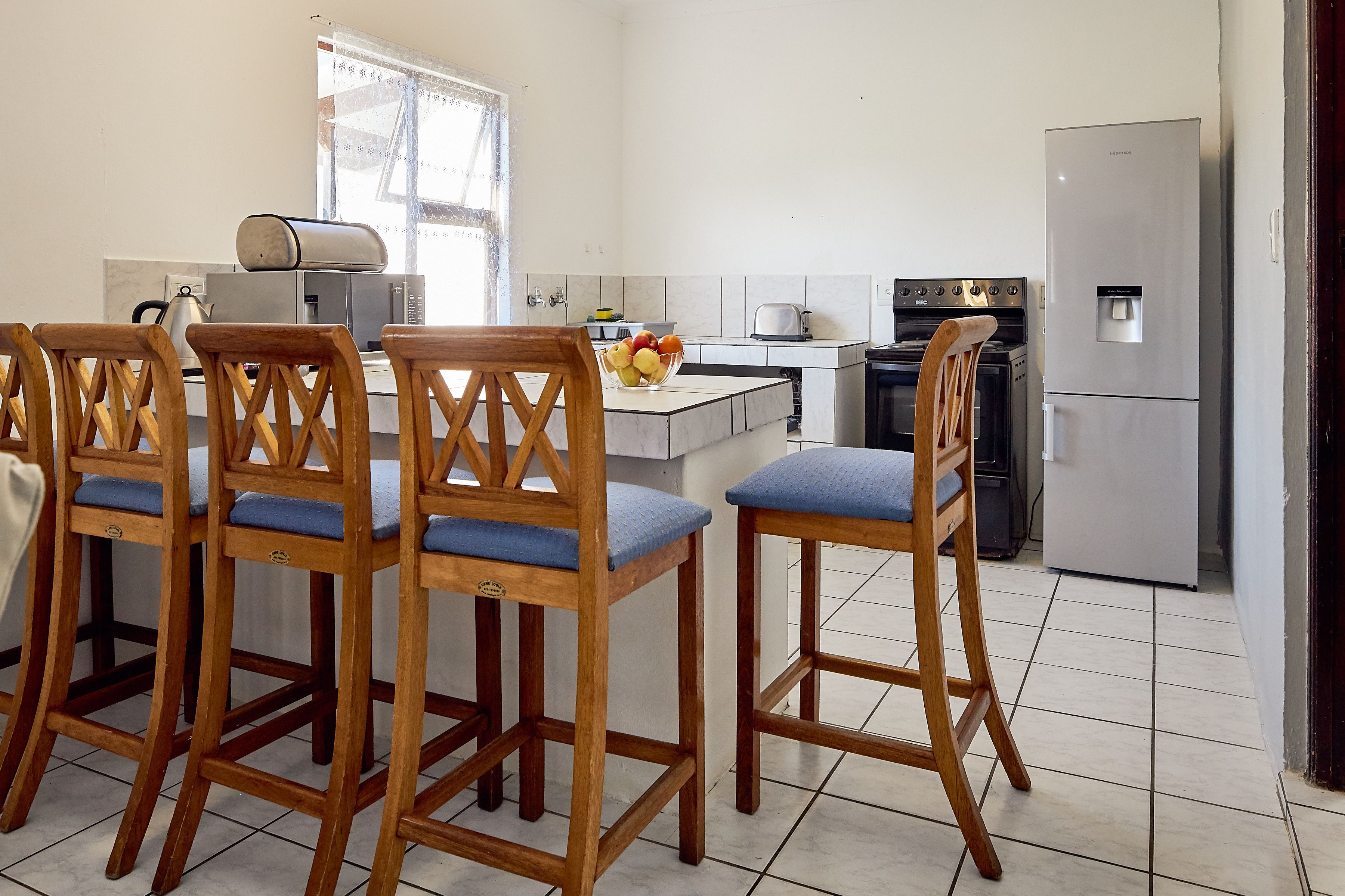 A kitchen with wooden bar stools, a refrigerator, a stove, and a microwave.