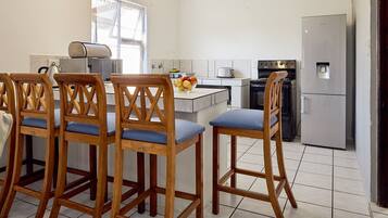 A kitchen with wooden bar stools, a refrigerator, a stove, and a microwave.