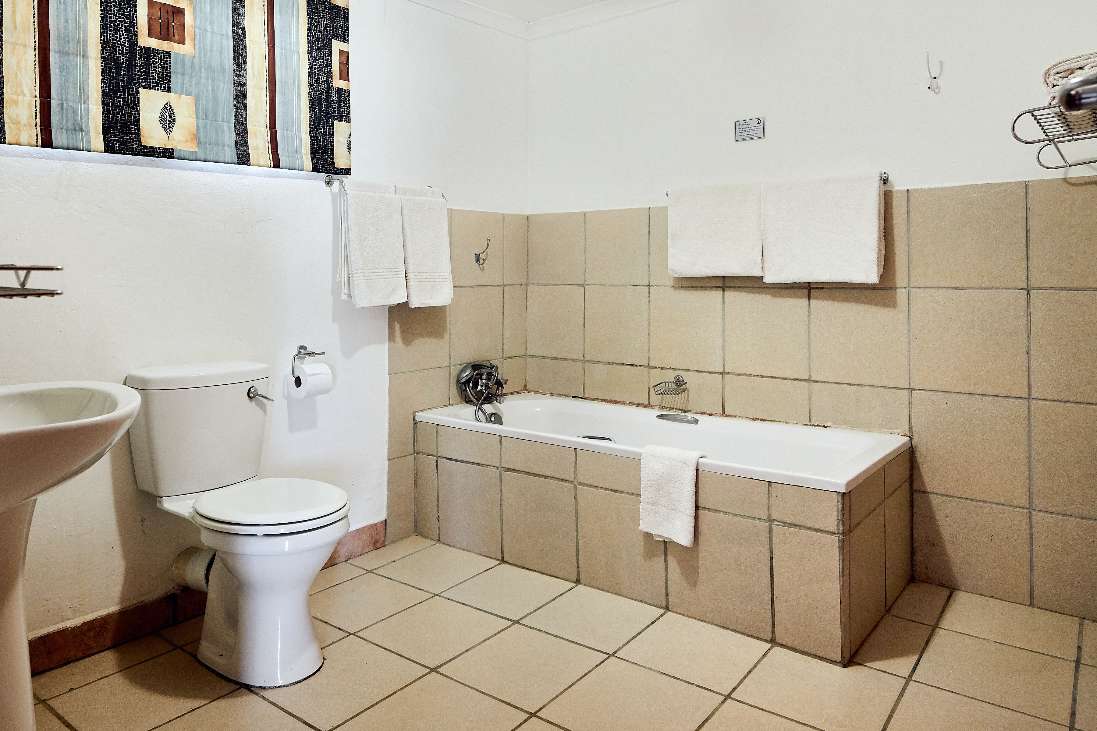 A bathroom with a toilet, sink, and bathtub. There are towels hanging on the wall.