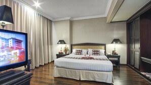 Een hotelkamer met een groot bed, twee nachtkastjes met lampen, een televisie op een standaard en uitzicht op de stad door het raam.