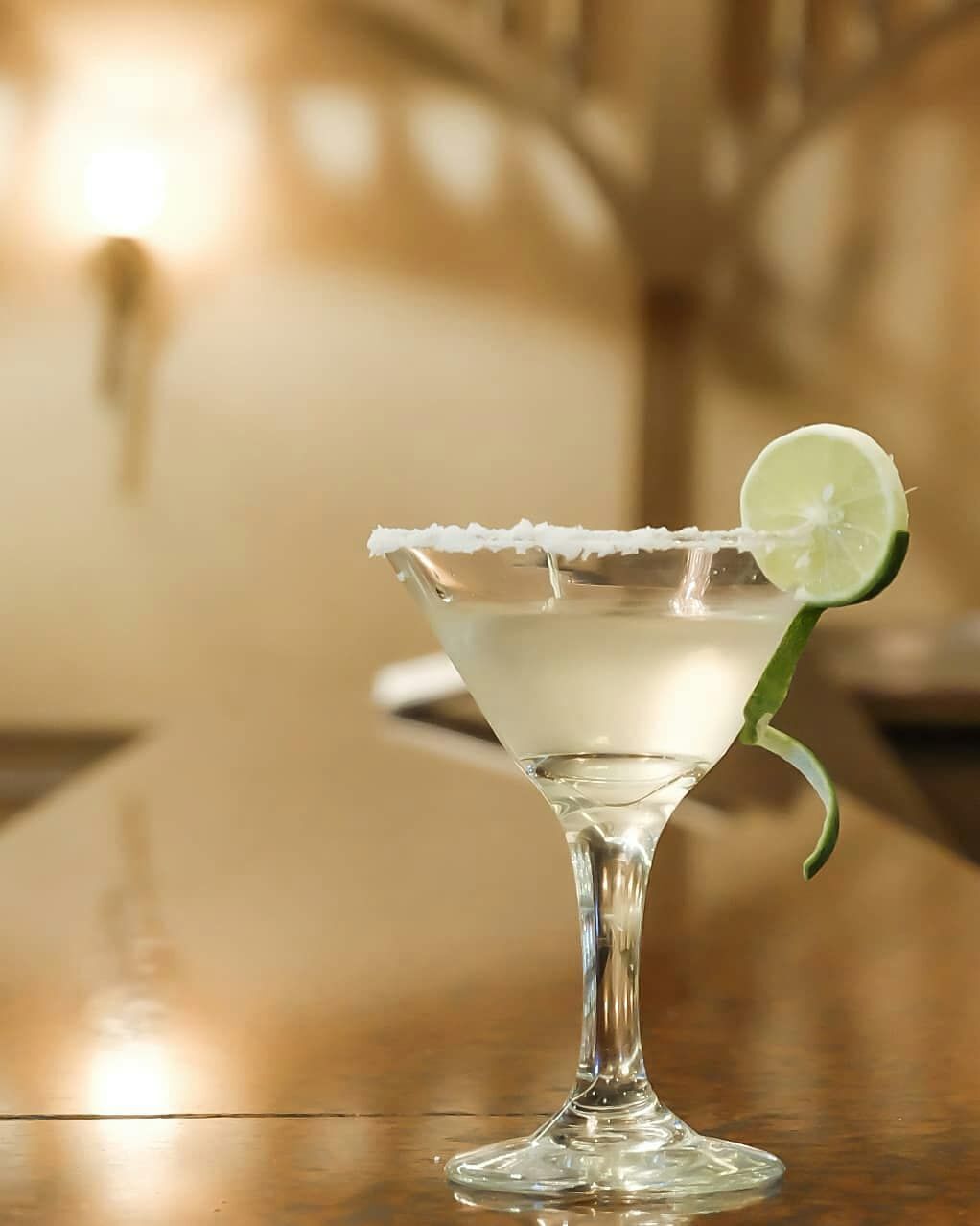 A clear glass margarita with a lime garnish on a bar counter.