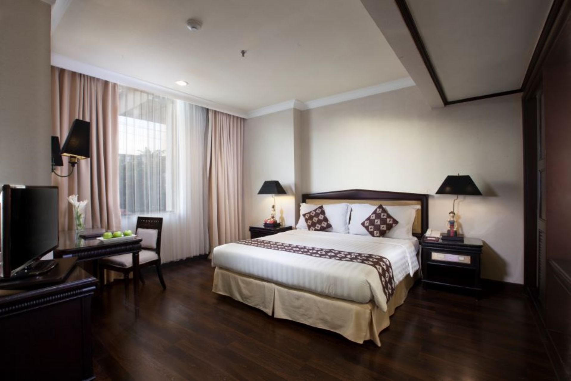 A hotel room with a large bed, two bedside tables, a desk with a chair, a television, and a window with curtains.