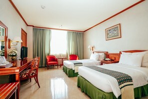 Quarto de hotel com duas camas, uma escrivaninha com cadeira, uma mesinha e uma televisão.