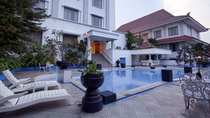 Een hotel met een zwembad, ligbedden en potplanten.