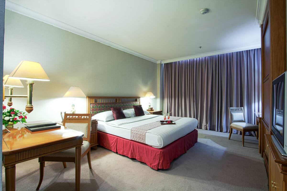 Une chambre d’hôtel avec un grand lit, un bureau avec une chaise, une télévision et une fenêtre avec des rideaux.