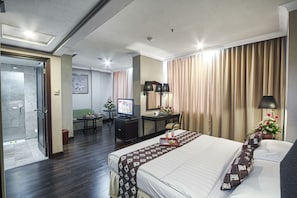 Quarto de hotel com cama, escrivaninha, televisão e banheiro.