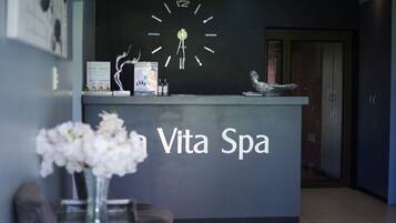 Un comptoir d’accueil avec une horloge, un vase de fleurs et une enseigne indiquant « Vita Spa ».