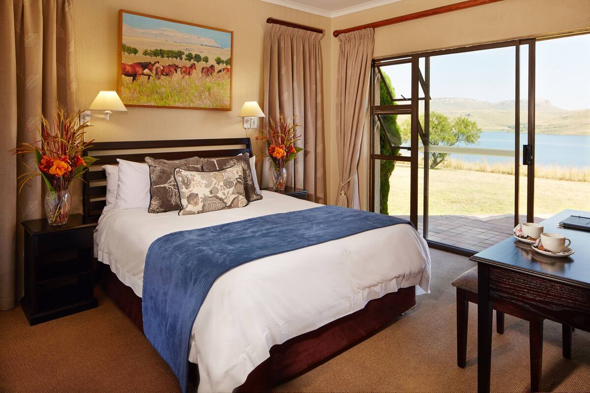A hotel room with a large bed, a desk, and a view of a lake.