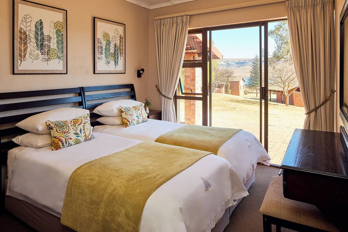 A hotel room with two beds, a piano, and a large sliding glass door leading to an outdoor area.